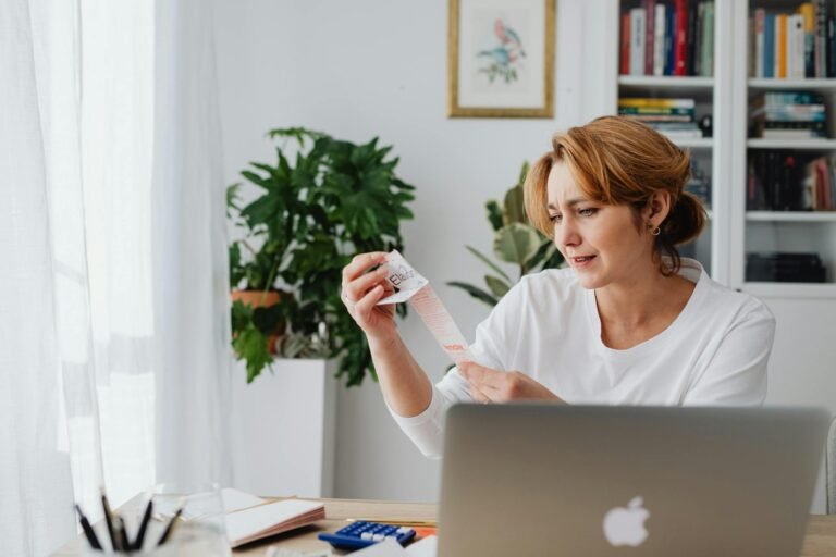 A woman in a white shirt sits indoors, examining a lengthy receipt with a concerned expression.