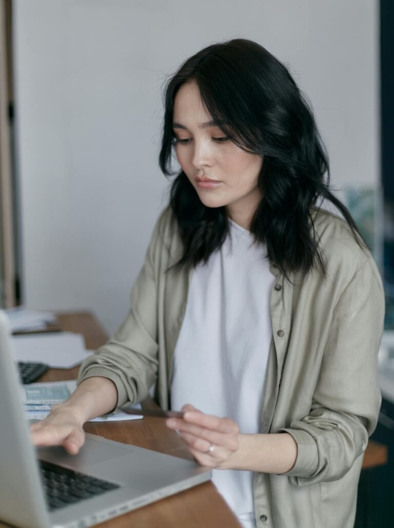 Focused young woman working on a laptop at her desk, managing finances.