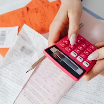 Hands using a pink calculator to manage expenses amidst various receipts and documents.