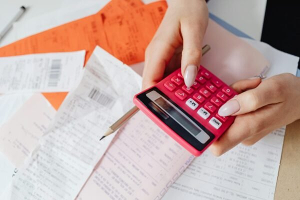 Hands using a pink calculator to manage expenses amidst various receipts and documents.